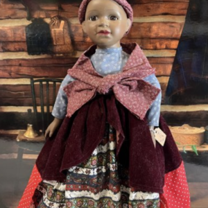 Inez, a 14-inch porcelain doll with a red patterned headscarf, velvet shawl, and blue floral blouse, set against a rustic cabin backdrop.